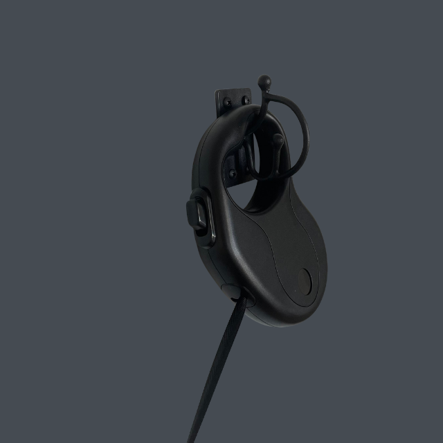 Black wired over-ear headset with microphone boom, hanging on a wall hook against a dark gray background.